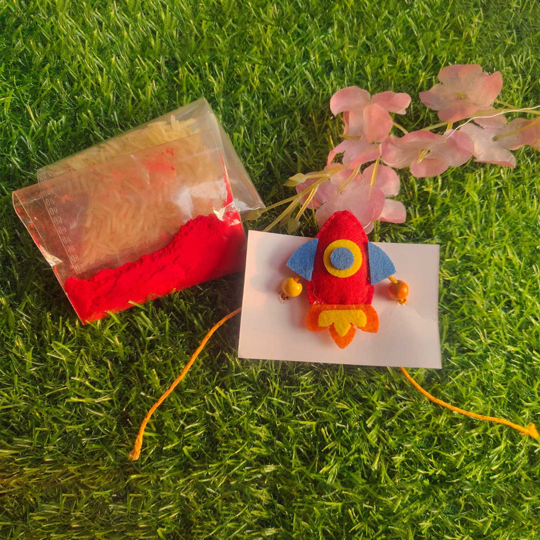 Handmade Beaded Rocket Theme Felt Rakhi With Roli Chawal For Kids - With Accessories on Grass