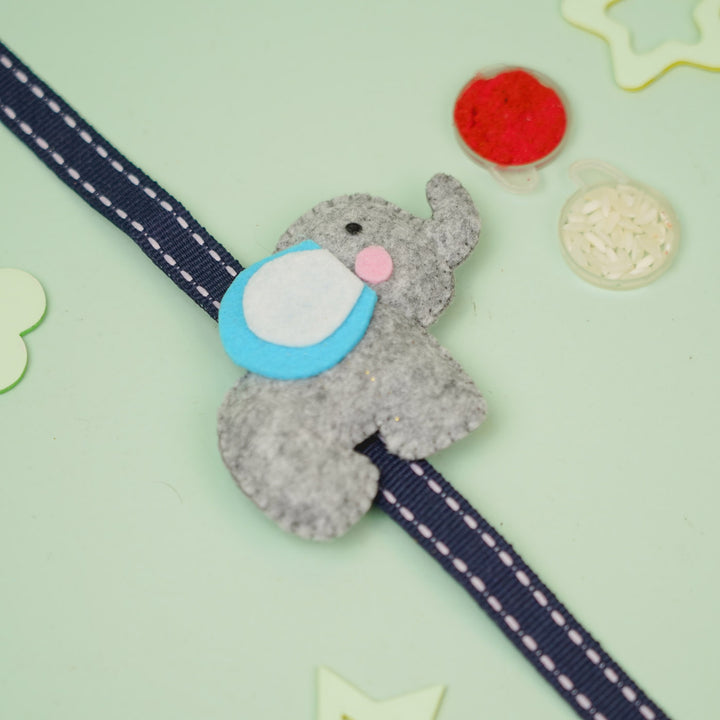 Handmade Elephant Theme Felt Kids Rakhi With Roli Chawal - Diagonal View on Gray Elephant Ornament