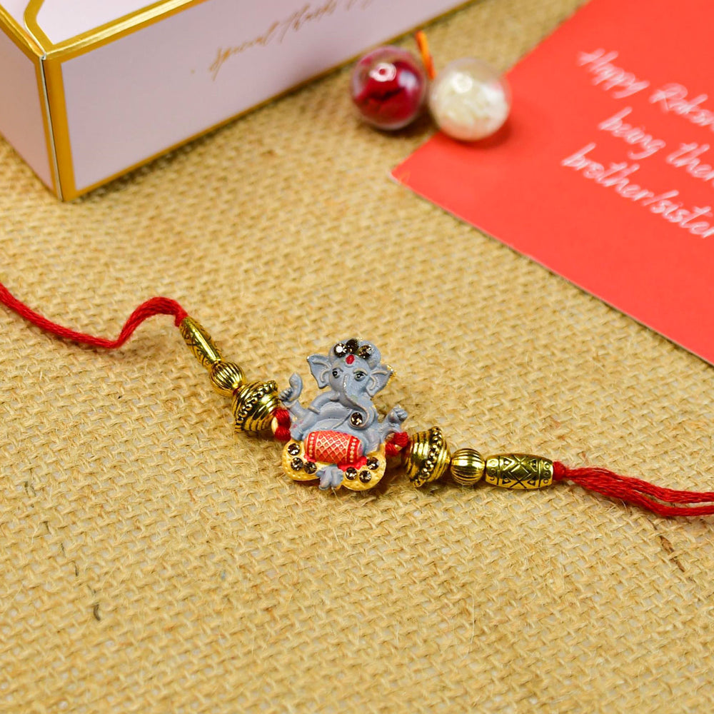 Beaded Ganesha Rakhi With Chocolates And Roli Chawal For Brother Customizable Options Includes Up To 7 Goodies - Full view of rakhi on burlap
