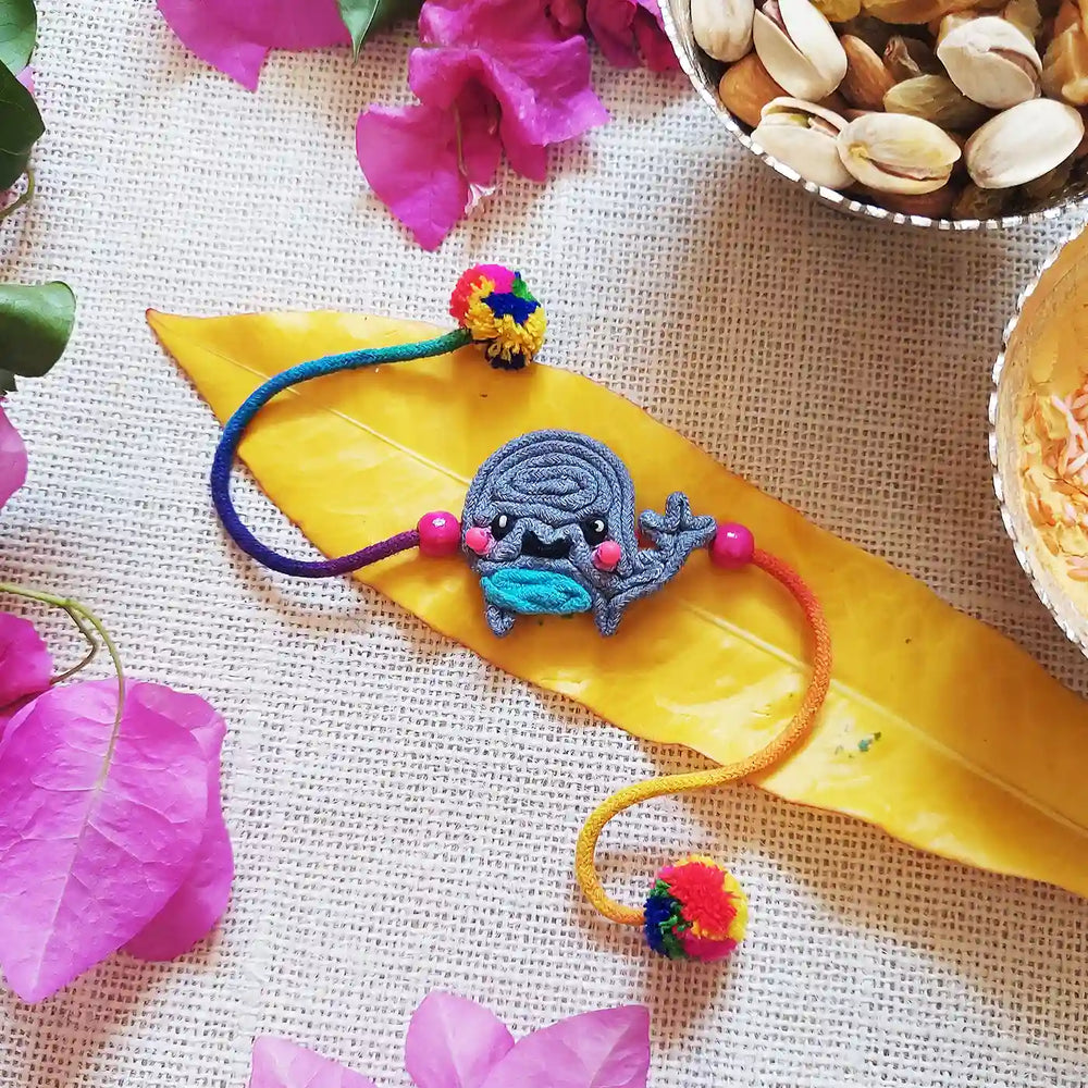 Handmade Dori Work Baby Whale Kids Rakhi With Roli Chawal - Styled Flat Lay with Accessories