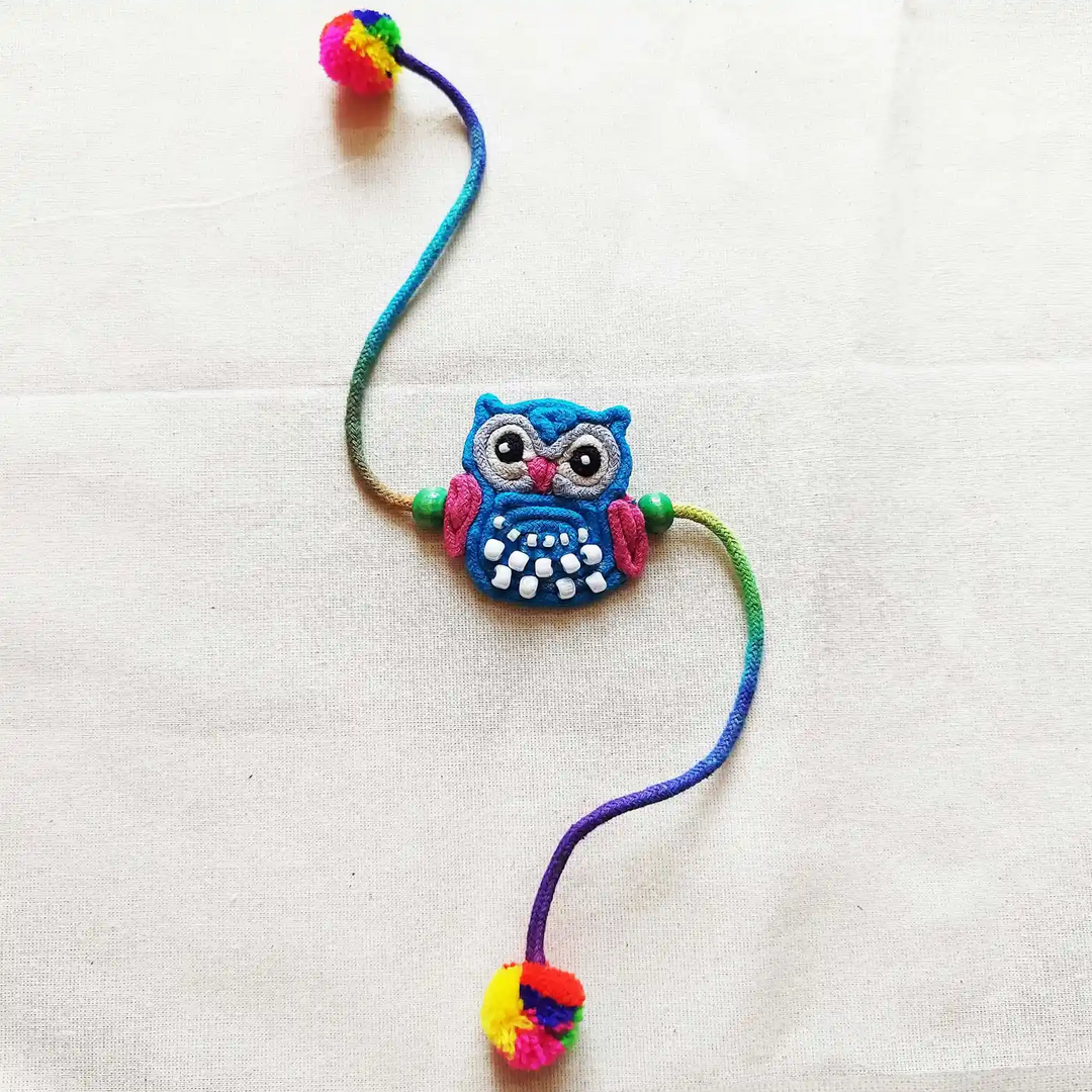Handmade Dori Work Beaded Blue Owl Kids Rakhi With Roli Chawal - Flat Lay on Plain Background