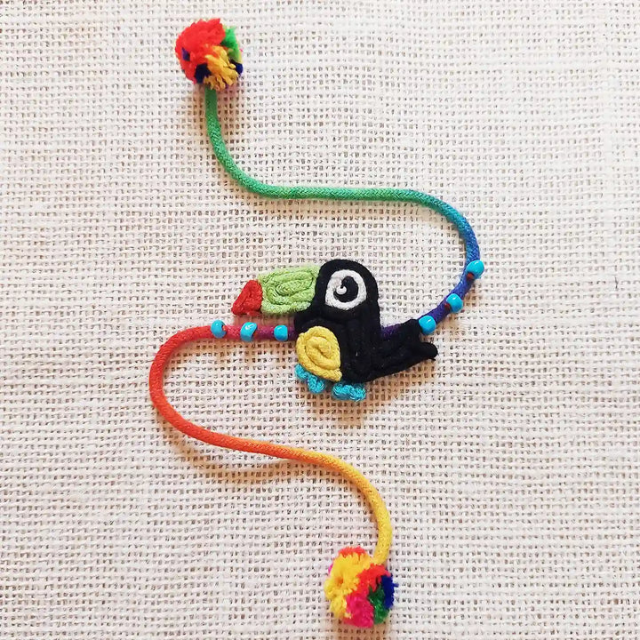 Handmade Dori Work Toucan Kids Rakhi With Roli Chawal - Flat Lay on Textured Fabric Background