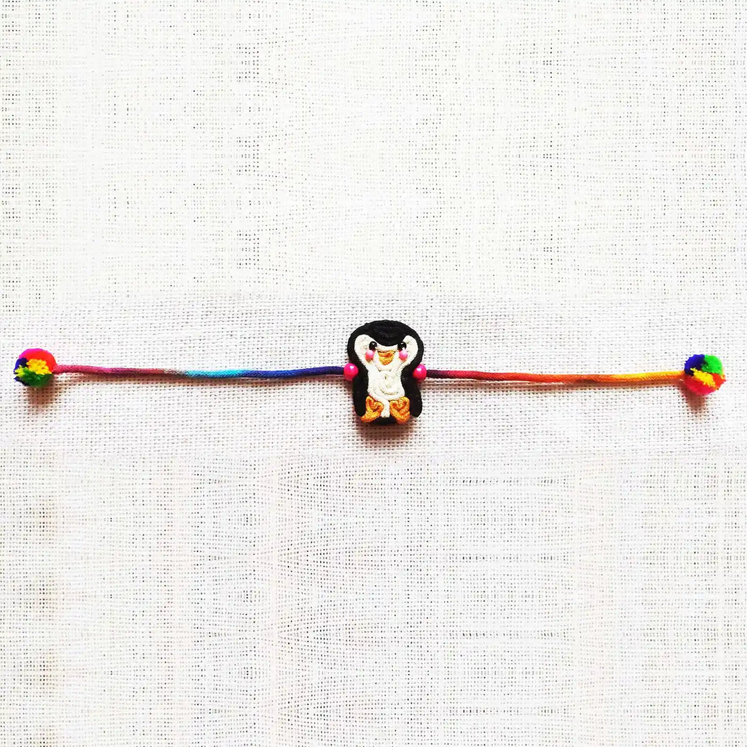 Handmade Dori Work Cute Penguin Kids Rakhi With Roli Chawal - Full Length Laid Flat View