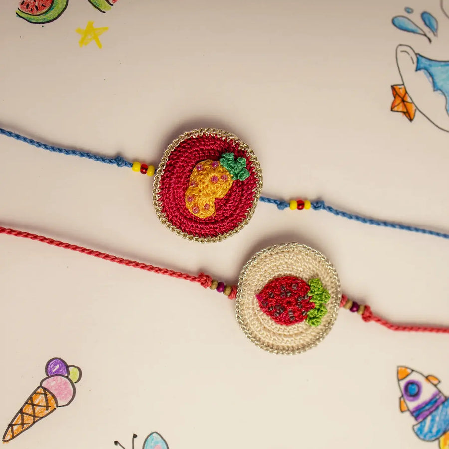 Handmade Crochet Pineapple And Strawberry Theme Kids Rakhi With Roli Chawal Set Of 2 - Top View with Colorful Background