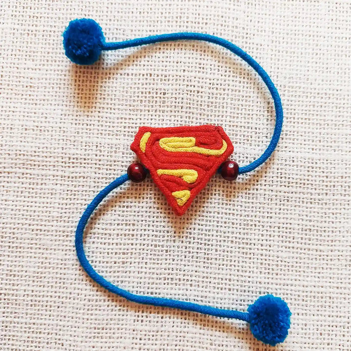 Handmade Dori Work Superman Kids Rakhi With Roli Chawal - Flat Lay on Textured Background