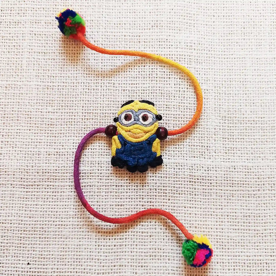 Handmade Dori Work The Minion Kids Rakhi With Roli Chawal - Close-up on Textured Background