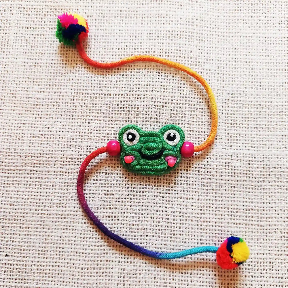 Handmade Dori Work Frog Kids Rakhi With Roli Chawal - Flat Lay on Textured Surface
