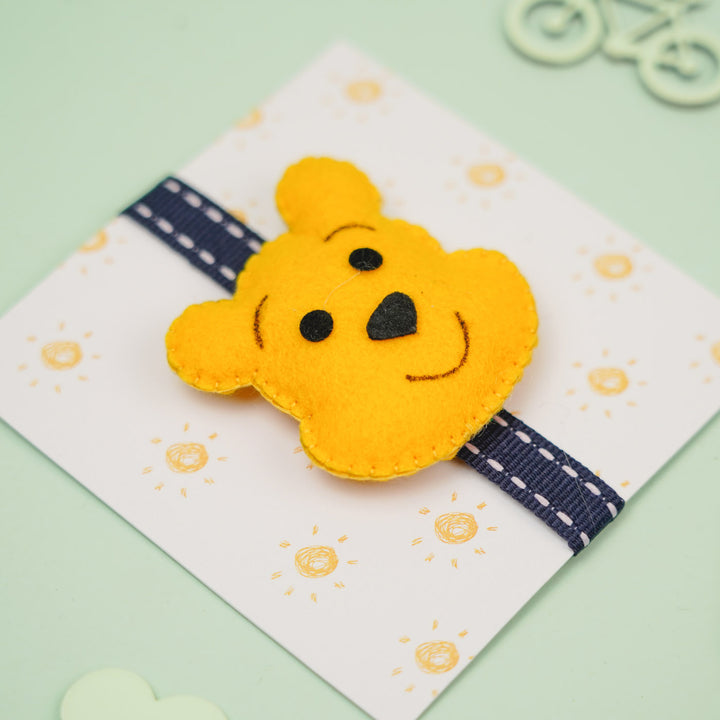 Handmade Pooh Theme Felt Kids Rakhi With Roli Chawal - Angled Front View on Cardboard