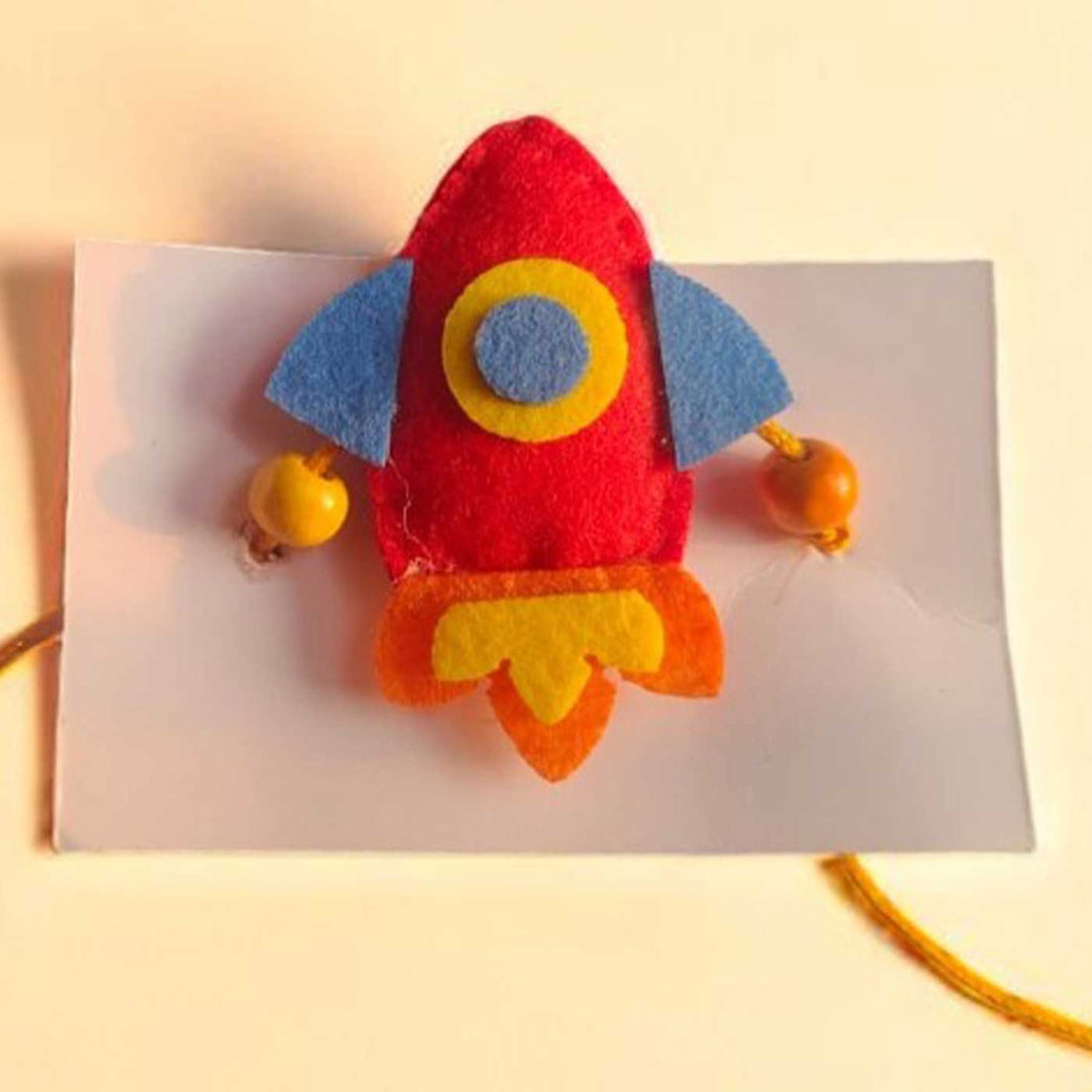 Handmade Beaded Rocket Theme Felt Rakhi With Roli Chawal For Kids - Close-up Front View on Cardboard