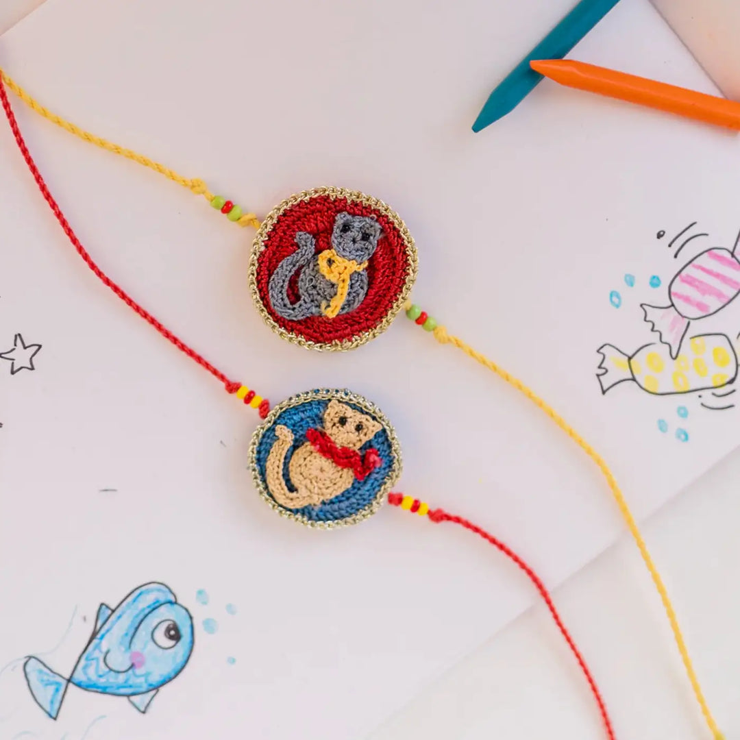 Handmade Crochet Kitten Theme Kids Rakhi With Roli Chawal Set Of 2 - Angled Flat Lay on Art Paper