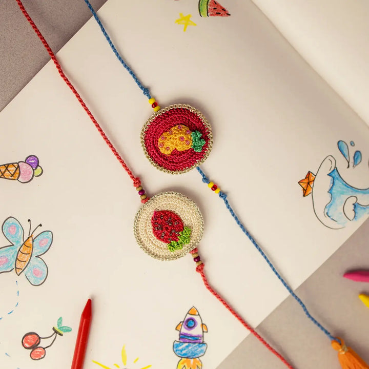 Handmade Crochet Pineapple And Strawberry Theme Kids Rakhi With Roli Chawal Set Of 2 - Close-up on Open Notebook Pages