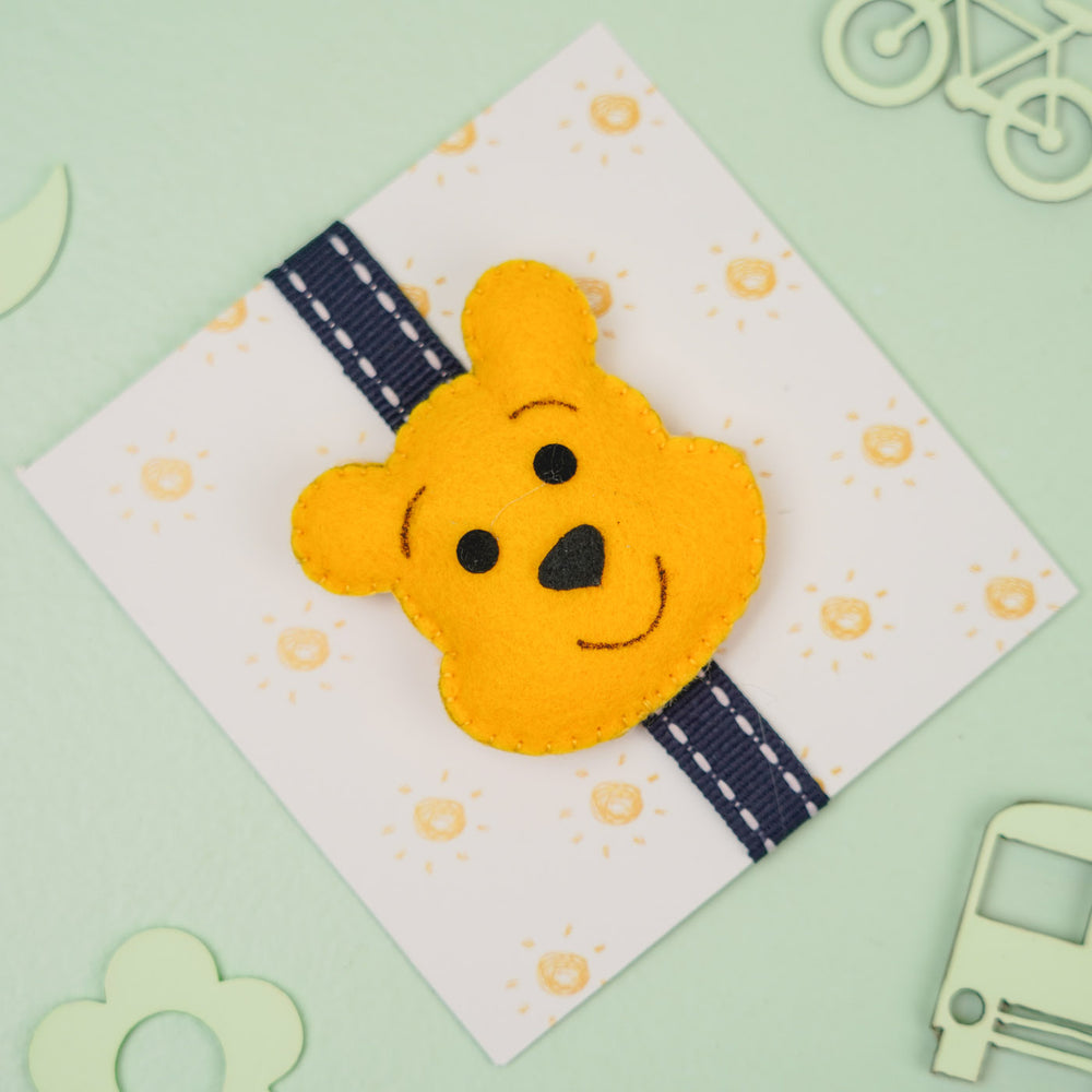 Handmade Pooh Theme Felt Kids Rakhi With Roli Chawal - Front View on Cardboard