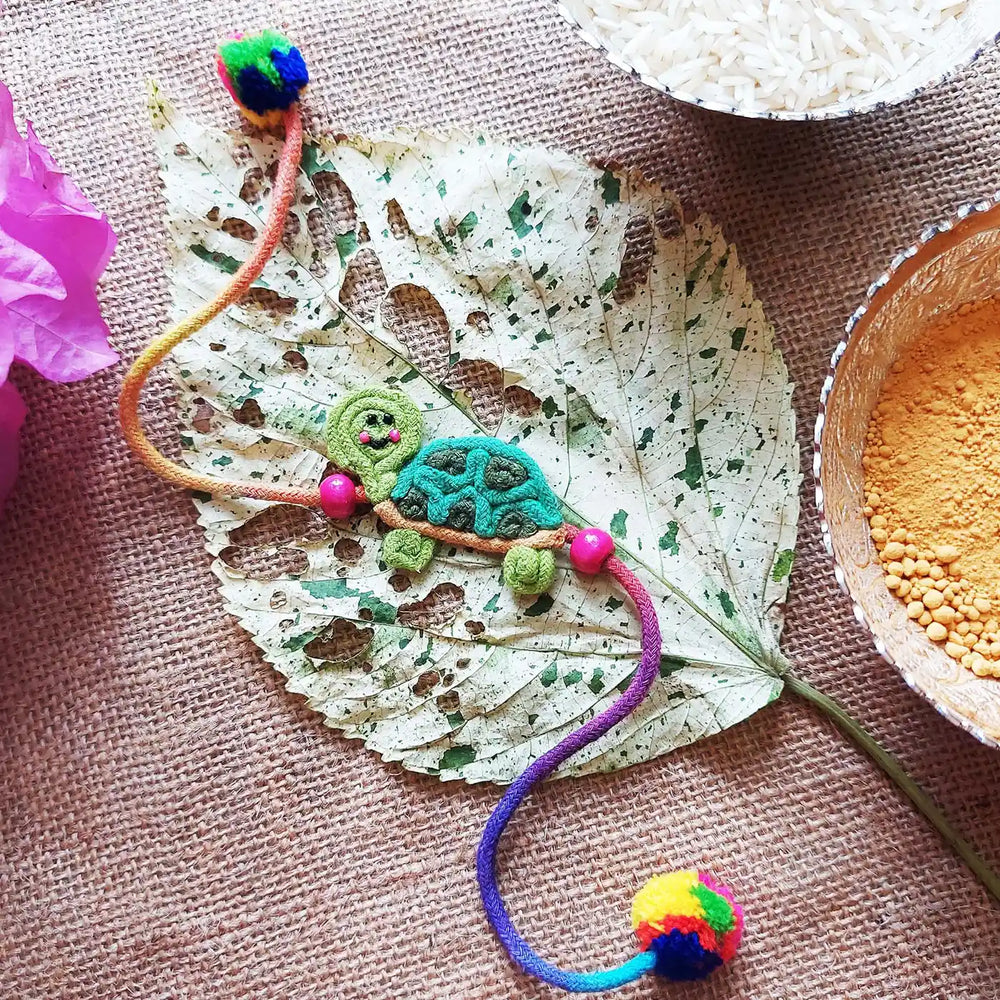 Handmade Dori Work Cute Tortoise Kids Rakhi With Roli Chawal - Styled Flat Lay Display