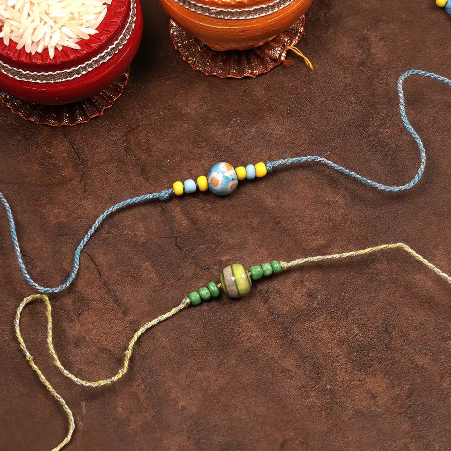 Handmade Blue Pottery Bead Rakhi With Roli Chawal Set Of 2 - Laid Flat with Decor Background