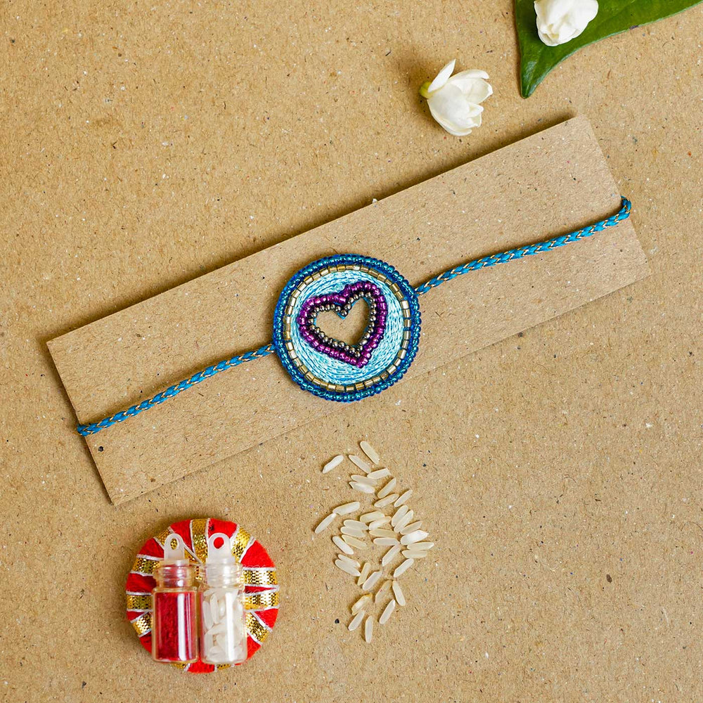 Handmade Beaded Heart Rakhi With Roli Chawal - Bracelet on cardboard with accessories