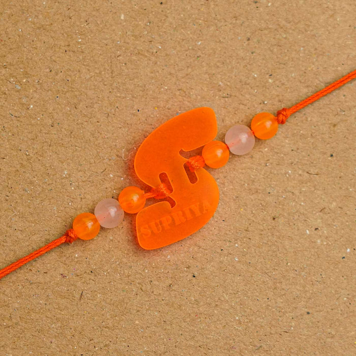 Personalized Handmade Alphabet Name Acrylic Rakhi With Roli Chawal - Close-up of Orange Rakhi