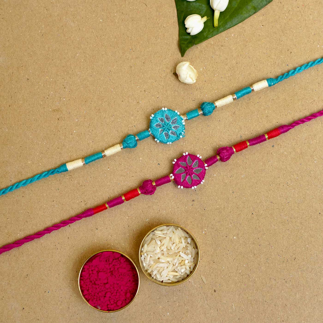 Handmade Mirror Work Patwa Turquoise Blue Pink Cotton Rakhi With Roli Chawal Set Of 2 - Flat lay with rice and powder