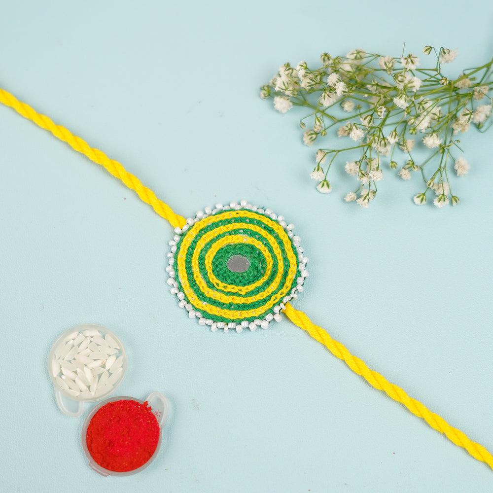 Handmade Reusable Yellow And Green Mirror And Jhumki Cotton Rope Rakhi For Brother - Flat Lay with Decorative Elements