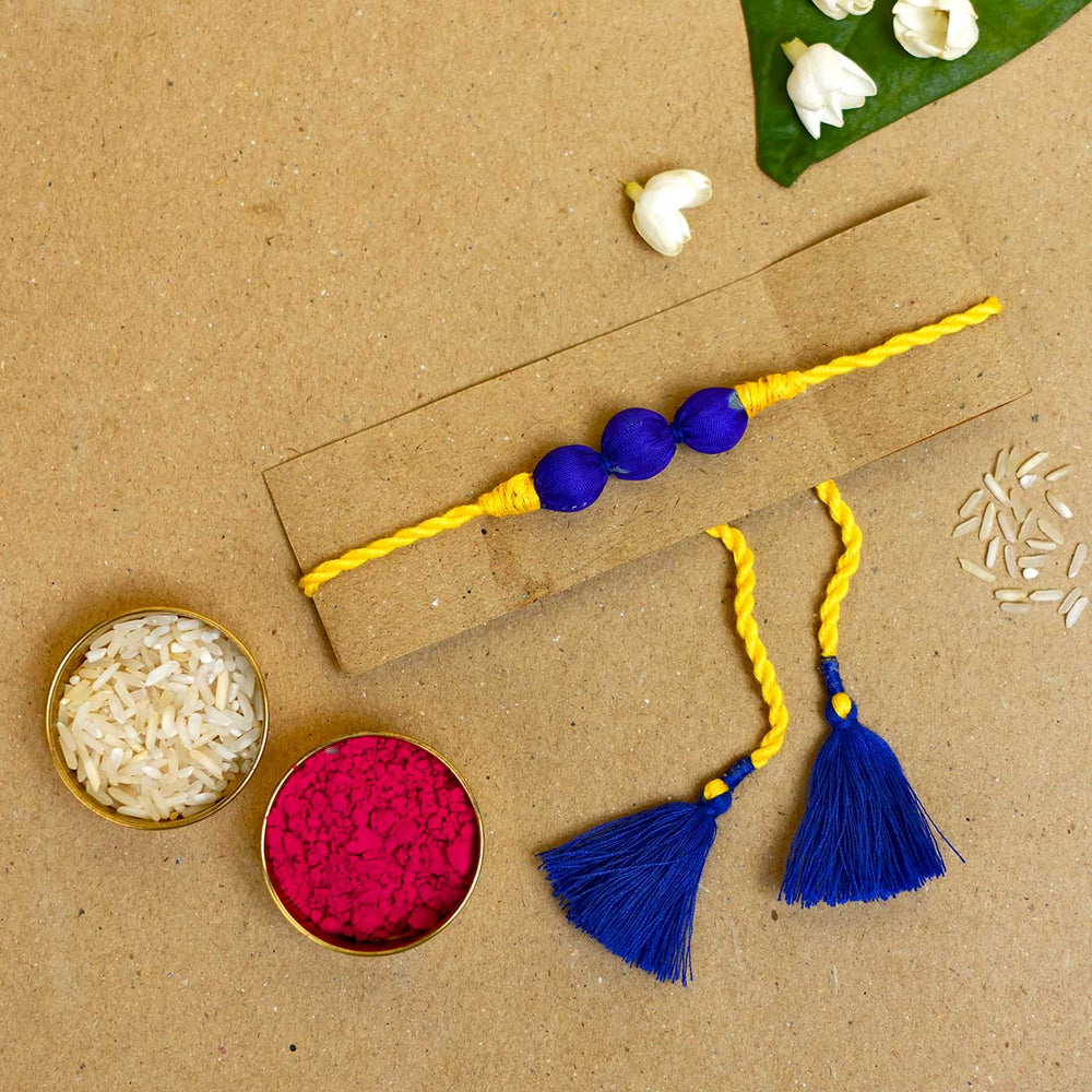 Handmade Bright Yellow Upcycled Fabric Rakhi With Roli Chawal - Flat lay with rice and kumkum bowls