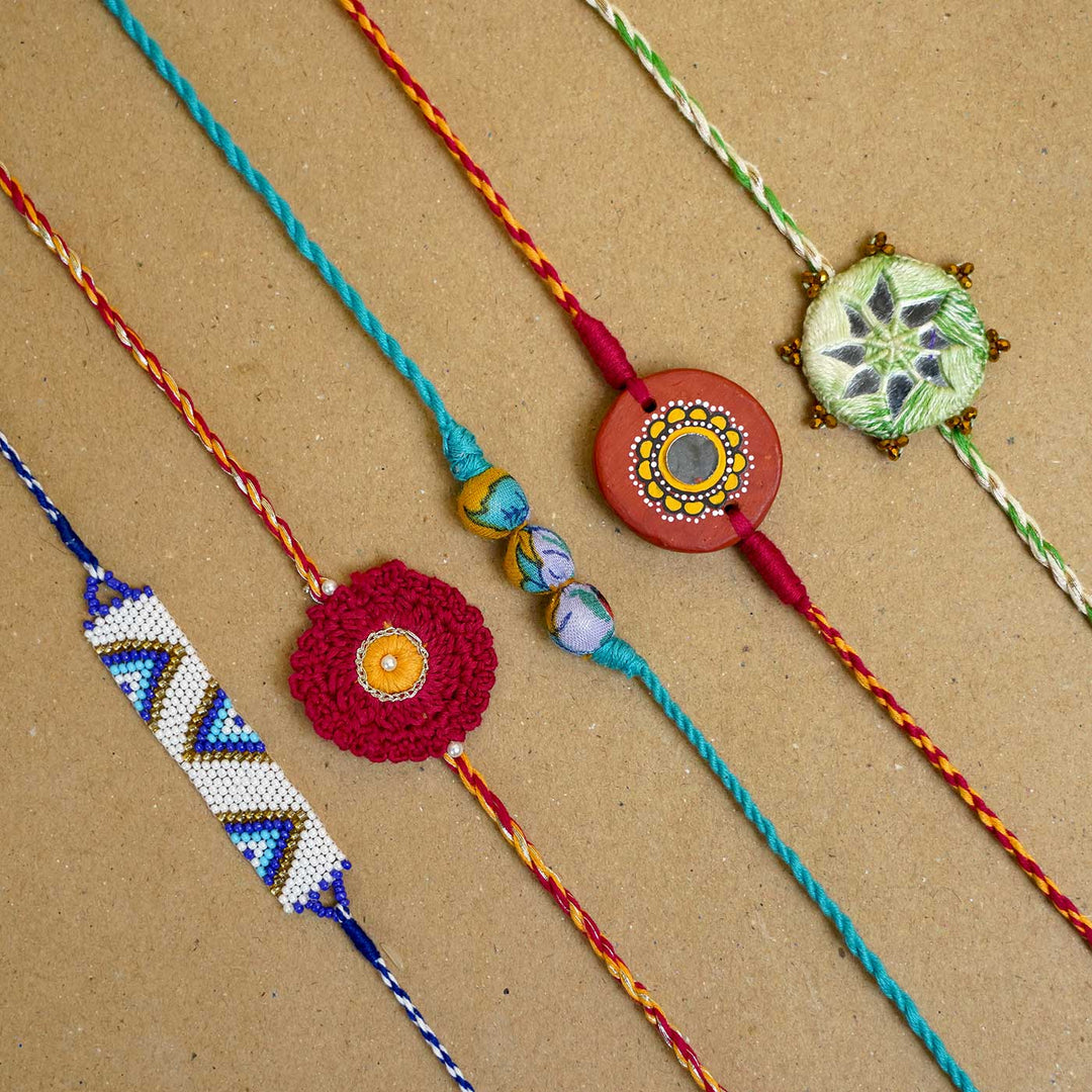 Handmade Mirror Work Patwa Maroon Green Cotton Rakhi With Roli Chawal Set Of 2 - Variety of rakhis laid flat