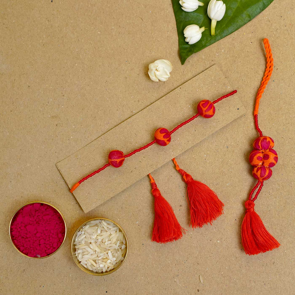 Handmade Kesari Potli Upcycled Fabric Bhaiya Bhabhi Rakhi With Roli Chawal Set Of 2 - Bracelet laid flat with festive items