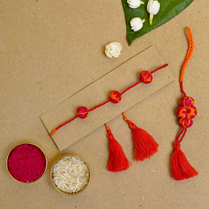 Handmade Kesari Potli Upcycled Fabric Bhaiya Bhabhi Rakhi With Roli Chawal Set Of 2 - Bracelet laid flat with festive items