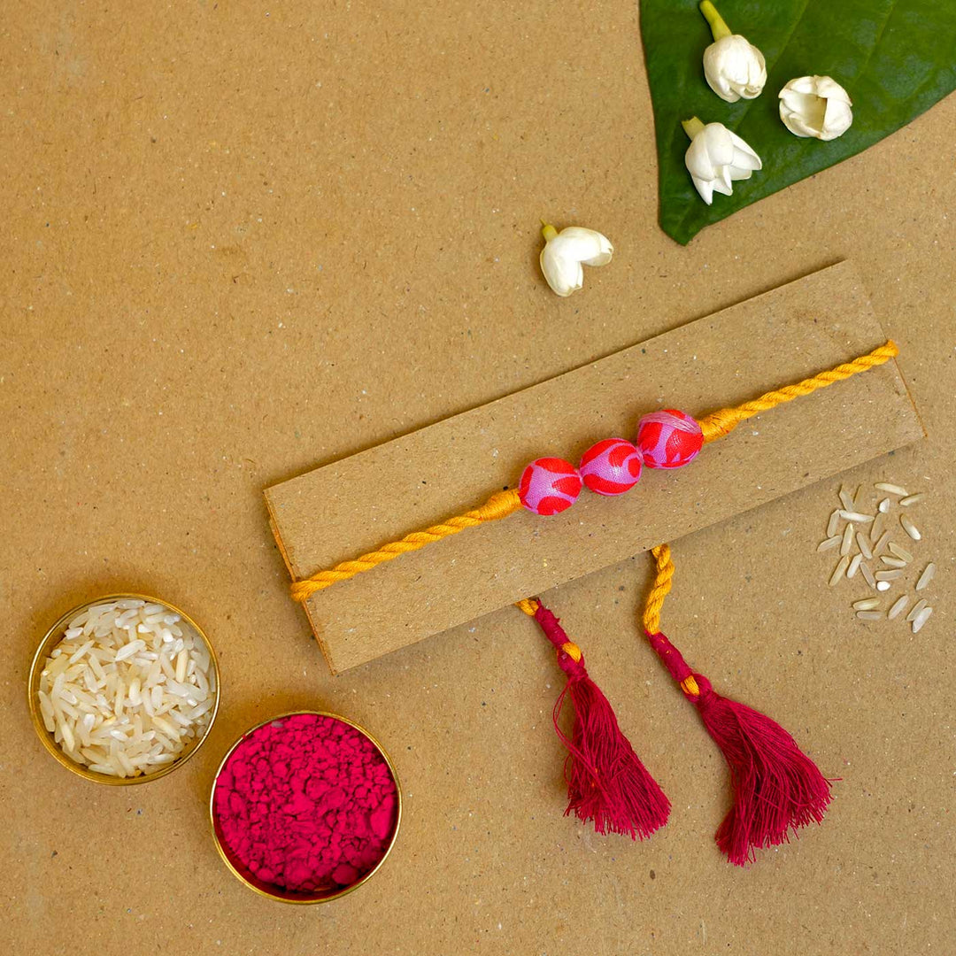 Handmade Ochre Upcycled Fabric Rakhi With Roli Chawal - Flat Lay with Holi Colors and Rice