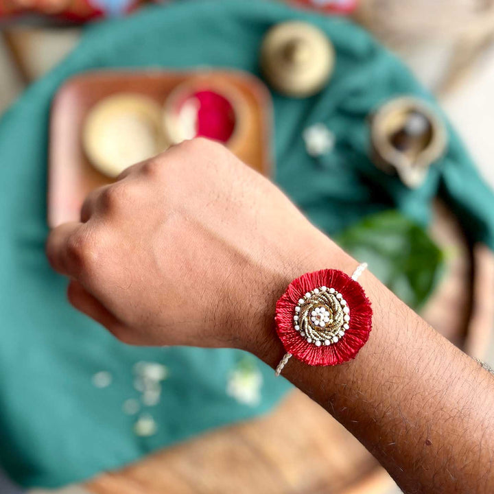 Handmade Zardozi Surajmukhi Rakhi With Wooden Box And Roli Chawal Set Of 2 - Close-up on wrist red