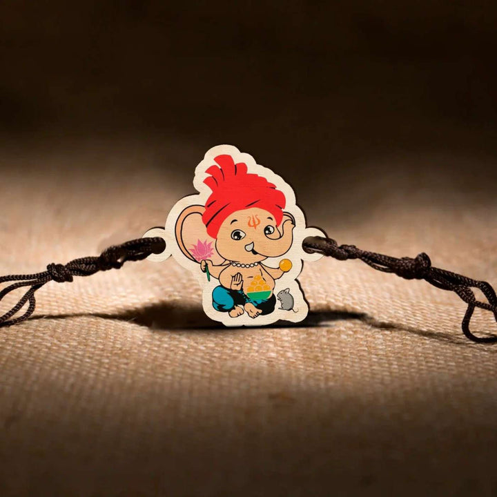 Handmade Ganapati Wooden Kids Rakhi With Roli Chawal - Rakhi displayed on textured fabric