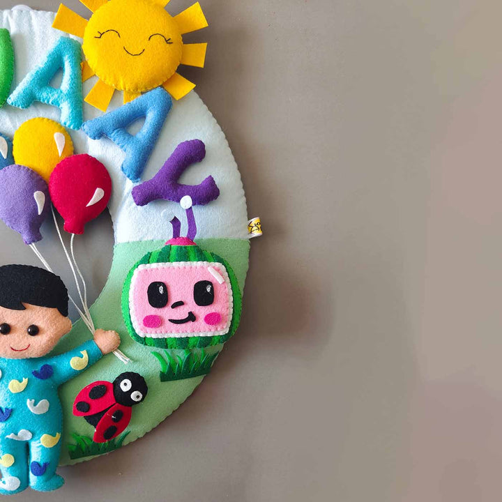 Hand Stitched Cocomelon Themed Round Felt Kids Name Plate For Baby Boy - Partial Front View on Wall
