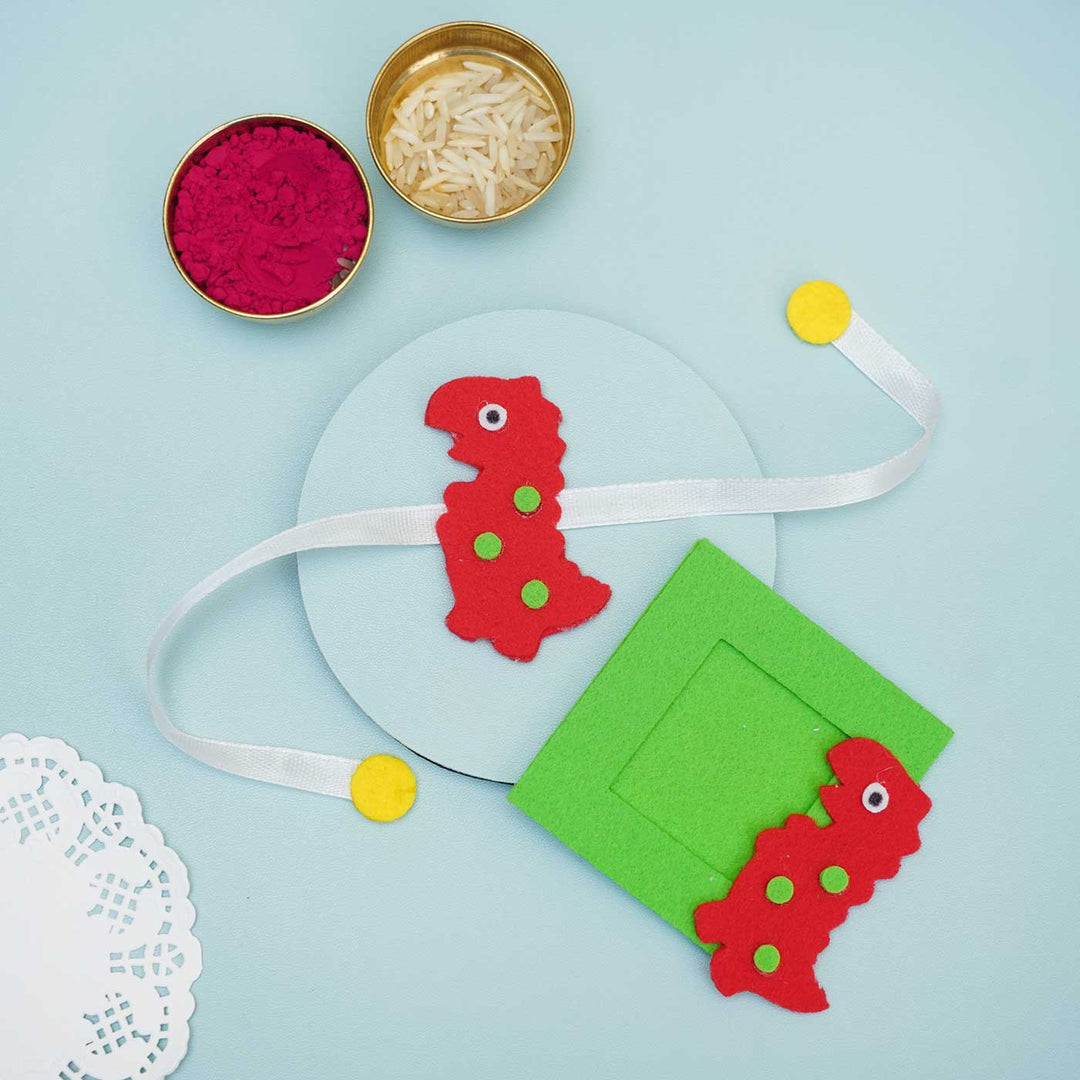 Handmade Red Dinosaur Felt Rakhi Photoframe Magnet With Chocolates Roli Chawal - Flat Lay with Rice and Color Powder