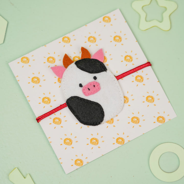 Handmade Squish Mallows Cow Theme Felt Kids Rakhi - Wrapped on Patterned Card, Angled View