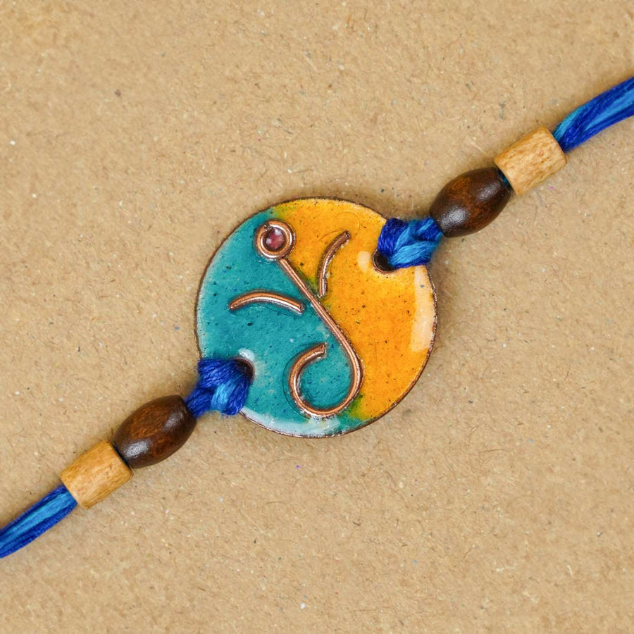 Handmade Round Ganesh Copper Enamel Rakhi With Chocolates And Roli Chawal - Close-up of blue-yellow bracelet centerpiece