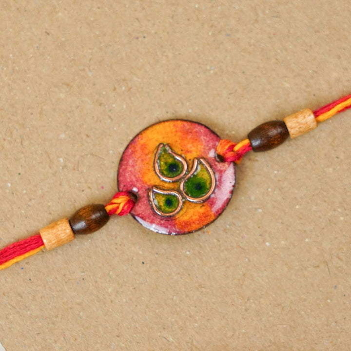 Handmade Morpankh Copper Enamel Rakhi With Chocolates And Roli Chawal - Close-up of red circular bracelet