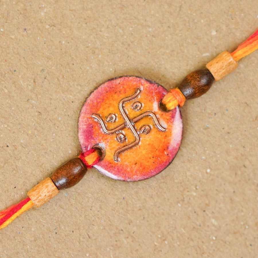 Handmade Swastika Copper Enamel Rakhi With Chocolates And Roli Chawal - Close-up of orange rakhi charm