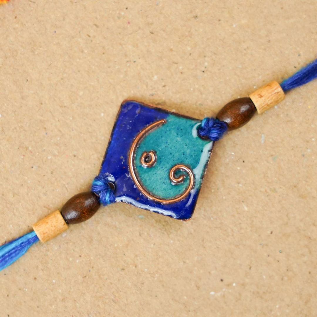Handmade Square Ganesh Copper Enamel Rakhi With Chocolates And Roli Chawal - Close-up of blue rakhi detail