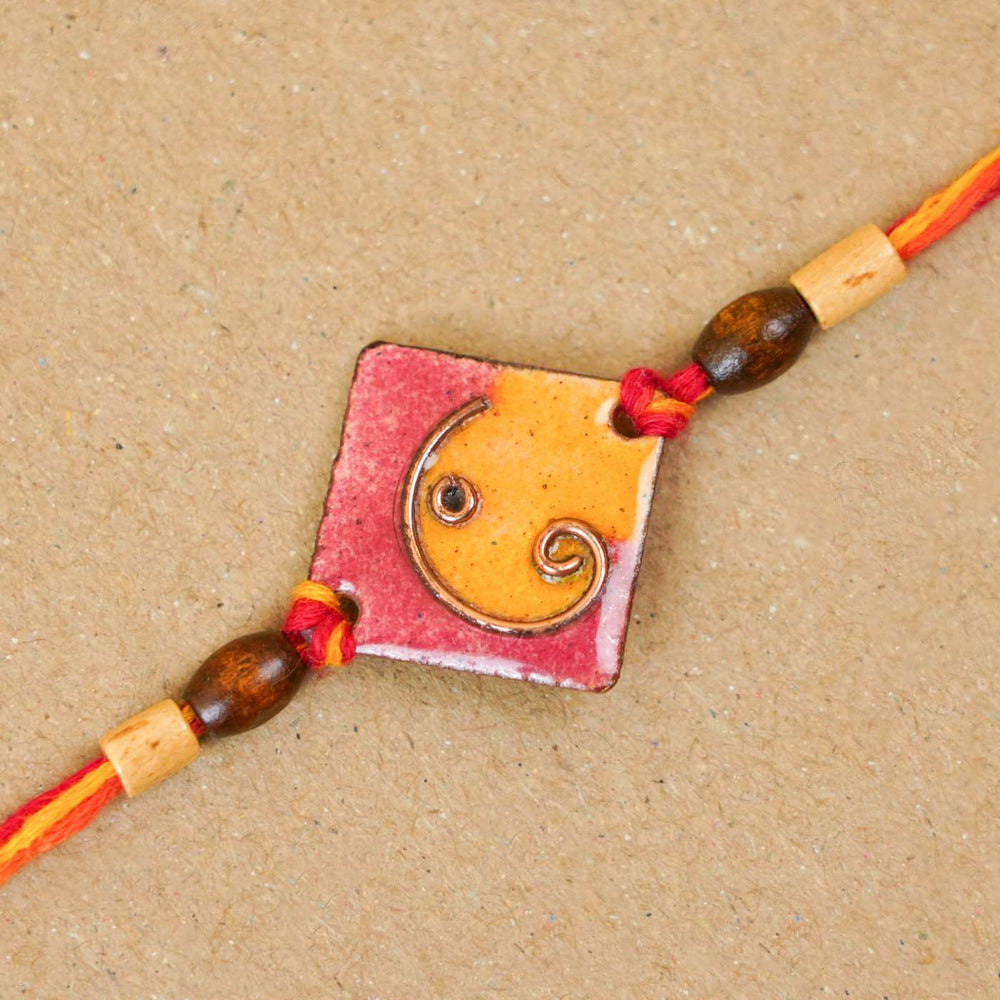 Handmade Square Ganesh Copper Enamel Rakhi With Chocolates And Roli Chawal - Close-up of orange rakhi detail