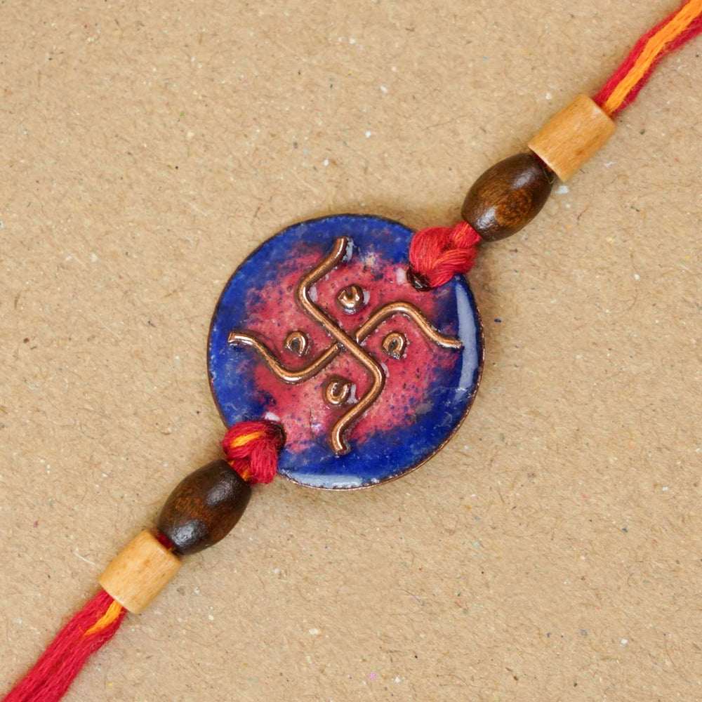 Handmade Swastika Copper Enamel Rakhi With Chocolates And Roli Chawal - Close-up of blue rakhi charm