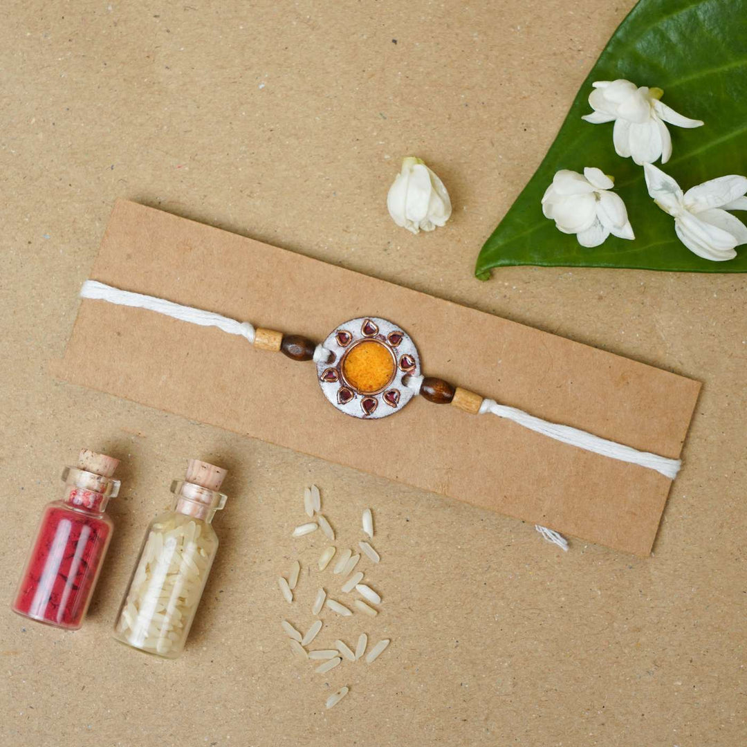 Handmade Sooraj White Copper Enamel Rakhi With Chocolates And Roli Chawal - Rakhi on cardboard holder