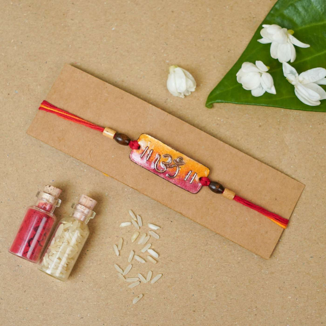 Handmade Rectangle Om Copper Enamel Rakhi With Chocolates And Roli Chawal - Mounted on Cardboard Display
