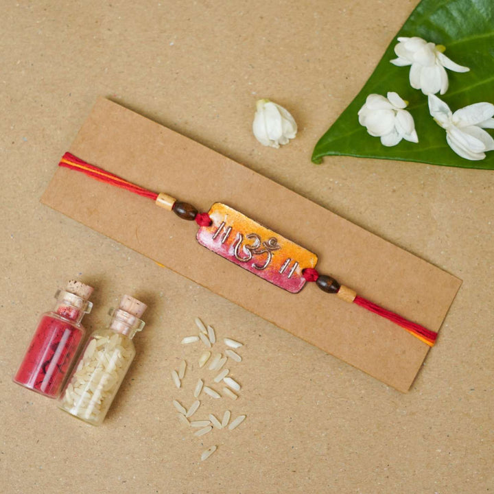 Handmade Rectangle Om Copper Enamel Rakhi With Chocolates And Roli Chawal - Mounted on Cardboard Display