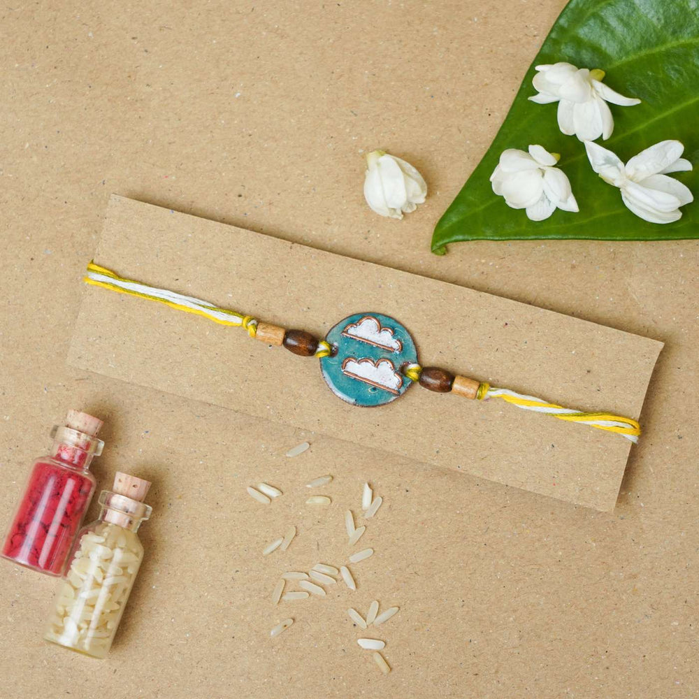 Handmade Baadal Blue Copper Enamel Rakhi With Chocolates And Roli Chawal - Flat lay of Rakhi on card