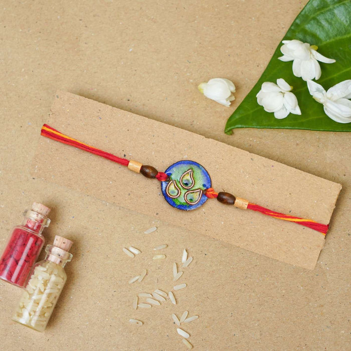 Handmade Morpankh Copper Enamel Rakhi With Chocolates And Roli Chawal - Blue bracelet on card with decoration