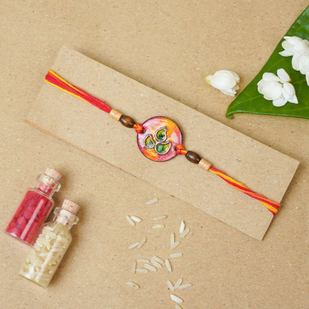 Handmade Morpankh Copper Enamel Rakhi With Chocolates And Roli Chawal - Red bracelet on card with decoration