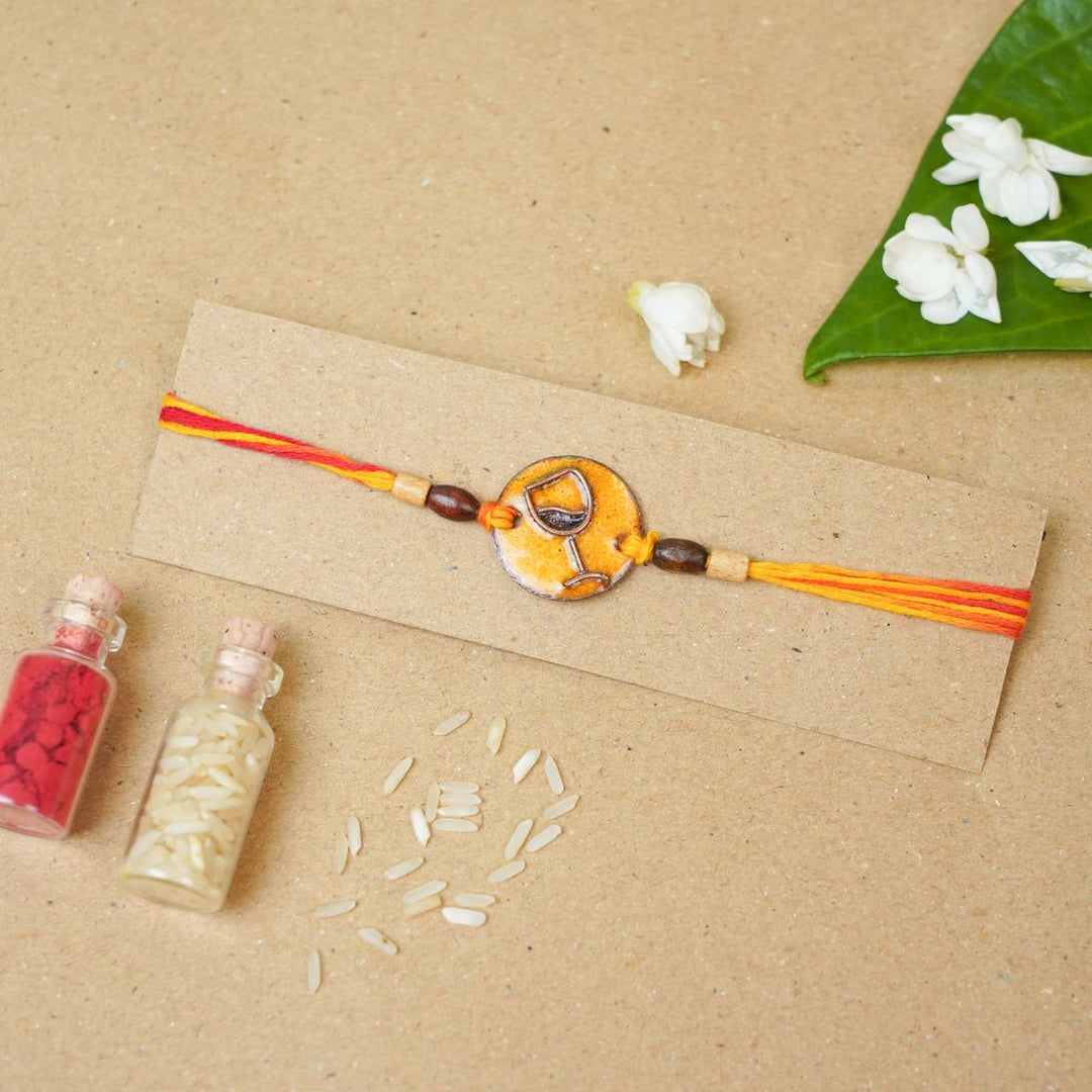 Handmade Wine O Clock Copper Enamel Rakhi With Chocolates And Roli Chawal - Bracelet displayed on packaging card