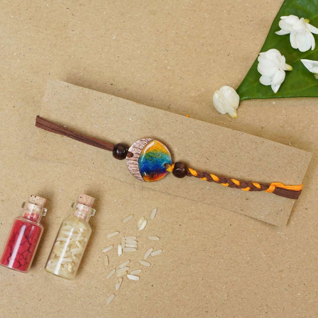 Handmade Indraa Textured Multicolour Copper Enamel Rakhi With Chocolates And Roli Chawal - Flat lay with decorative props
