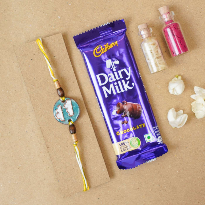 Handmade Baadal Blue Copper Enamel Rakhi With Chocolates And Roli Chawal - Rakhi next to chocolate bar