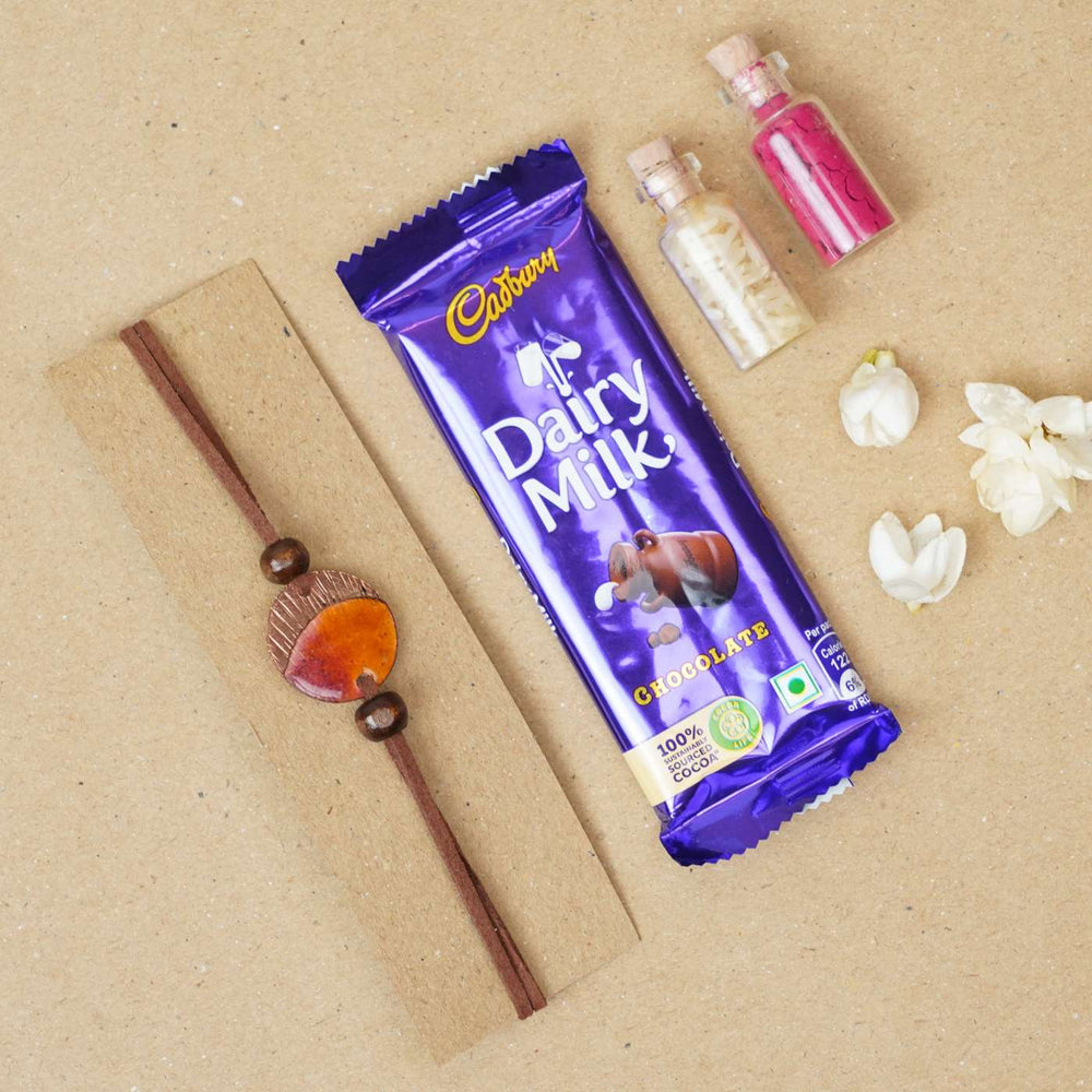 Handmade Ambar Textured Yellow Copper Enamel Rakhi With Chocolates And Roli Chawal - Flat Lay with Bracelet and Chocolate