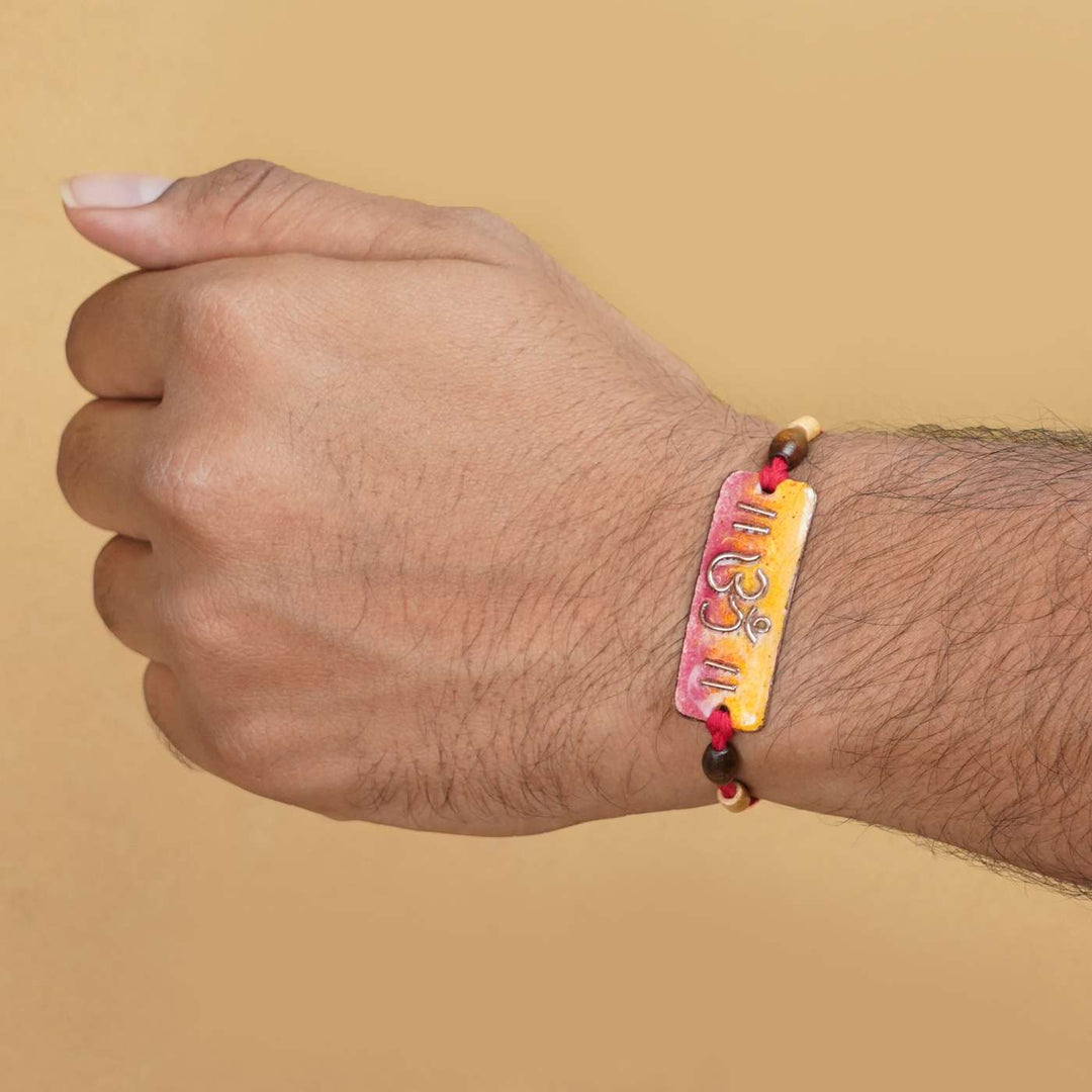 Handmade Rectangle Om Copper Enamel Rakhi With Chocolates And Roli Chawal - On Wrist Model Display