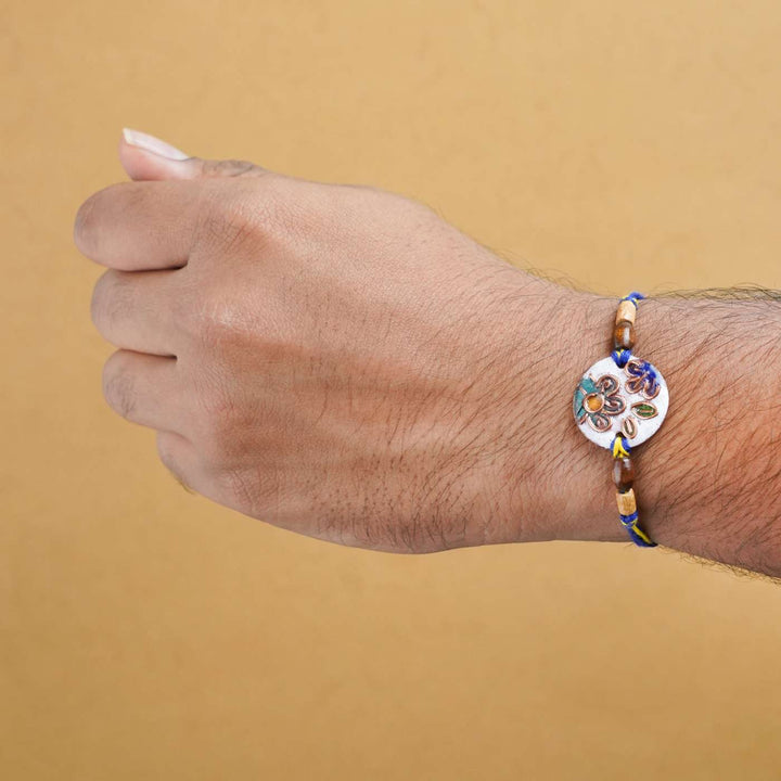 Handmade Phool White Copper Enamel Rakhi With Chocolates And Roli Chawal - Worn view on wrist